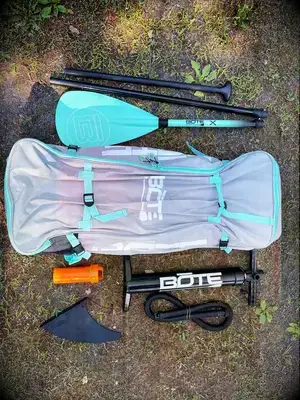 A person carrying the inflated Isle Pioneer 2.0 Paddle Board across rocks on the shore