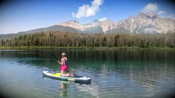 A person kneeling on the ROC Inflatable Stand Up Paddle Board in a lake
