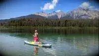 A person kneeling on the ROC Inflatable Stand Up Paddle Board in a lake
