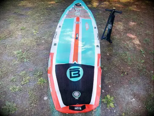 A person carrying a deflated SereneLife Inflatable Stand-up Paddleboard in its carrier 