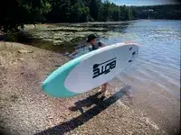 A person standing on the SereneLife Inflatable Stand-up Paddleboard while in a lake