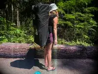 A person carrying a deflated SereneLife Inflatable Stand-up Paddleboard in its carrier 