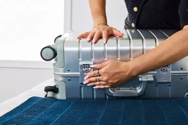 A person secures the latch on the side of the Away The Carry-on Aluminum Edition