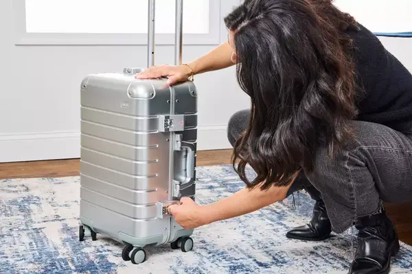 A person latches the lock on the Away The Carry-on Aluminum Edition