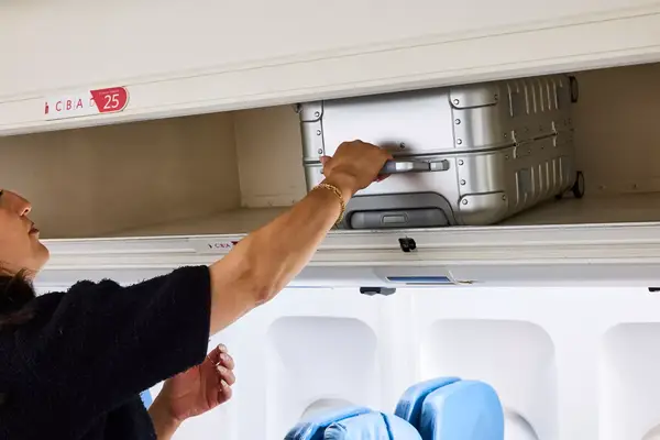 A person places the Away The Carry-on Aluminum Edition into an overhead compartment