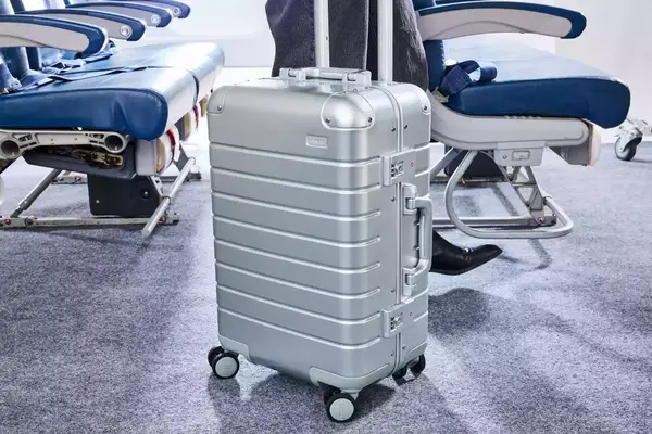 A person wheels the Away The Carry-on Aluminum Edition over carpet