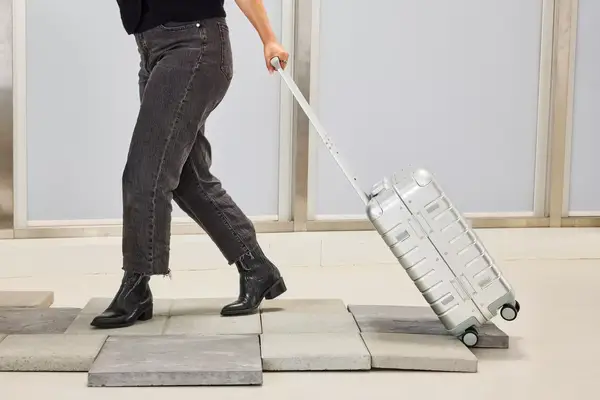 A person wheels the Away The Carry-on Aluminum Edition over stone pavers