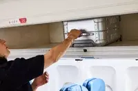 A person places the Away The Carry-on Aluminum Edition into an overhead compartment