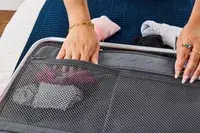 A person places socks into the mesh pocket of the Away The Carry-on Aluminum Edition