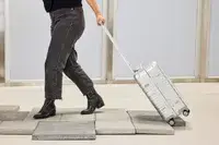 A person wheels the Away The Carry-on Aluminum Edition over stone pavers