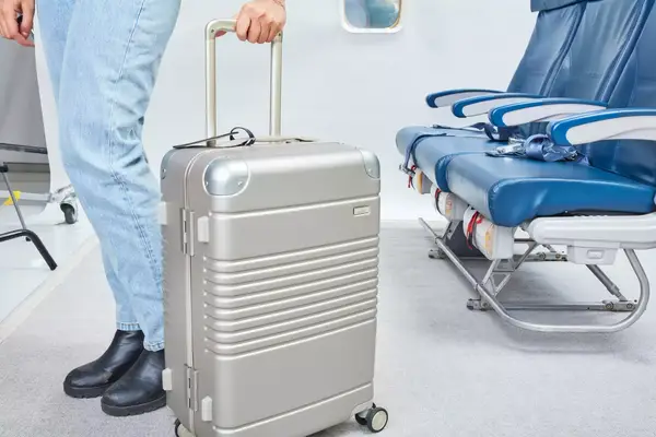 A person holds an Arlo Skye The Frame Carry-on in an airplane setting
