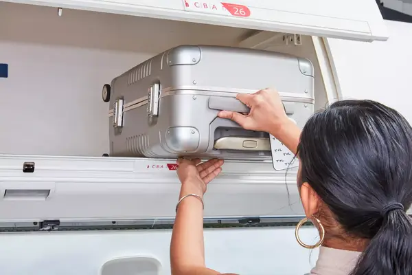 A person places an Arlo Skye The Frame Carry-on in an overhead compartment