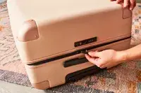 Hand unzipping the July Checked Plus Large Luggage