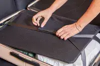 Hands strapping down clothing in the July Checked Plus Large Luggage