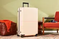 July Checked Plus Large Luggage displayed between a leather floor cushion and a chair