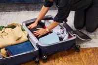 a person pressing items into a filled Travelpro Maxlite Air Medium Check-In Hardside Spinner