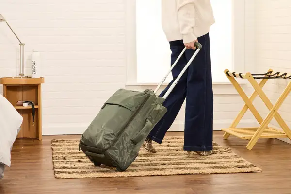 A person rolls the Lipault Foldable Plume Cabin over a rug