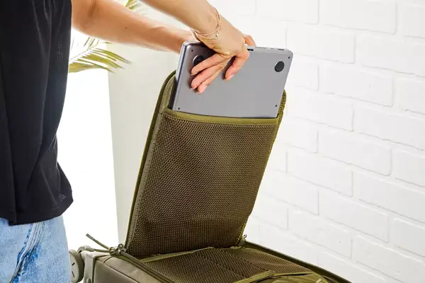 A person placing a laptop inside of a compartment in the Dagne Doverr Seattle Carry On Rolling Luggage 20.5