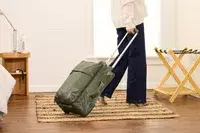 A person rolls the Lipault Foldable Plume Cabin over a rug
