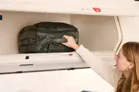 A person places the Lipault Foldable Plume Cabin into an overhead compartment