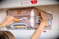 A person placing a Tumi carry-on in an overhead bin