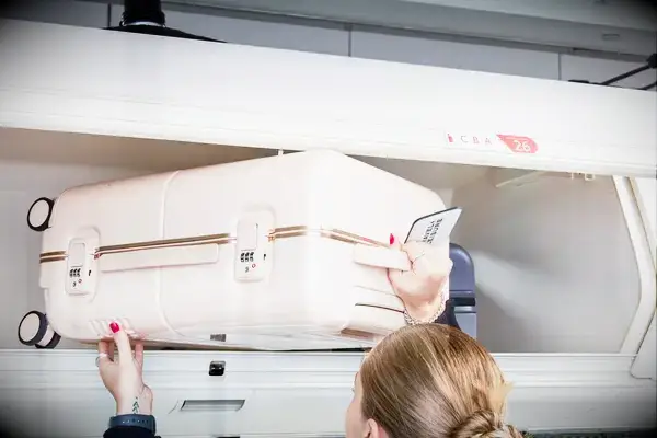 Hands putting July Carry On Trunk in the overhead bin of an airplane