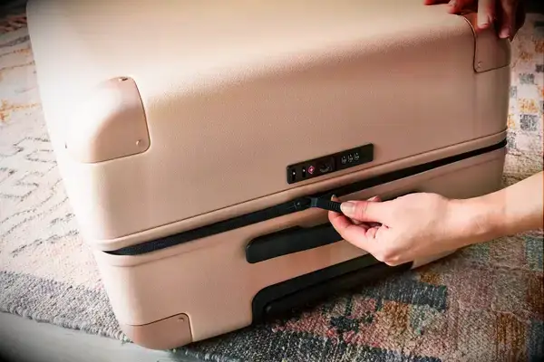 A person zipping a July suitcase