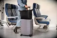 A person rolls the July Carry-on Max down an airplane aisle