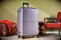 July Checked Plus Light suitcase next to a chair and table