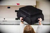 A person putting a Calpak Softside Carry-on into an overhead bin