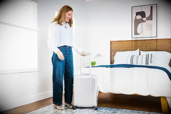 A person wheels the Rimowa Cabin S Hard Suitcase over a rug