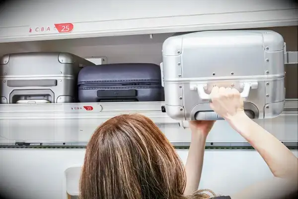 A person places the Away The Bigger Carry-On: Aluminum Edition into an overhead compartment