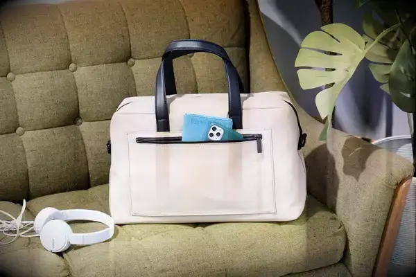 The Away The Everywhere Bag on a couch with headphones