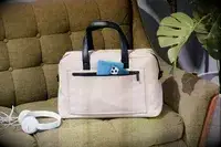 The Away The Everywhere Bag on a couch with headphones