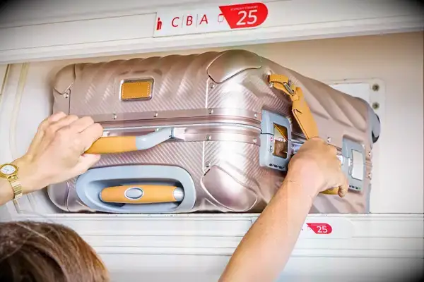 A person placing a Tumi carry-on in an overhead bin