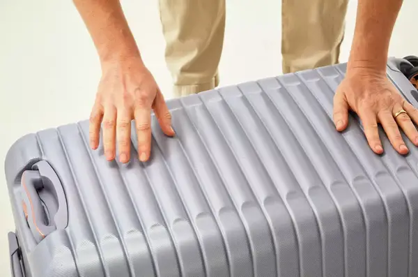 Two hands pushing the Delsey Paris Cruise 3.0 26 Inch Trunk closed