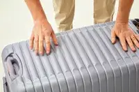 Two hands pushing the Delsey Paris Cruise 3.0 26 Inch Trunk closed