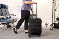 A person wheels the Delsey Paris Cruise 3.0 Soft Carry-On Expandable Spinner over carpet