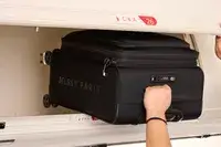 A person places the Delsey Paris Cruise 3.0 Soft Carry-On Expandable Spinner into an overhead compartment