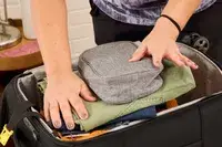 A person packs travel items in the Delsey Paris Cruise 3.0 Soft Carry-On Expandable Spinner