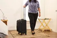 A person rolls the Delsey Paris Cruise 3.0 Soft Carry-On Expandable Spinner over a rug