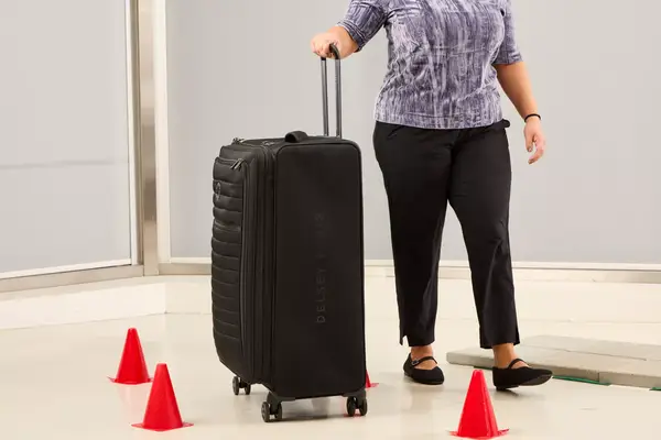 A person wheels the Delsey Paris Cruise 3.0 Soft Large Expandable Spinner over a floor