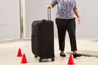 A person wheels the Delsey Paris Cruise 3.0 Soft Large Expandable Spinner over a floor