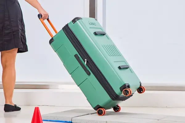 A person pulls the Delsey X Jeep JH002B Large Expandable Spinner Trunk over stone pavers