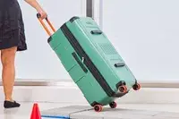 A person pulls the Delsey X Jeep JH002B Large Expandable Spinner Trunk over stone pavers