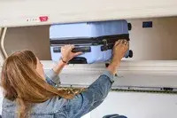 A person placing the DELSEY PARIS X United Colors of Bennetton Carry-on Spinner into an overhead bin