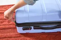 A hand holding the zipper of the DELSEY PARIS X United Colors of Bennetton Carry-on Spinner