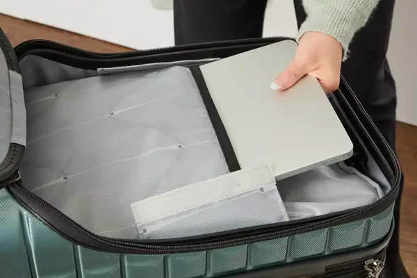 A person places a laptop into a pocket in the Delsey Paris Shadow 5.0 Carry-on with Laptop Compartment