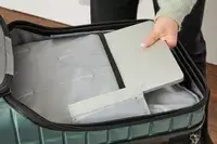 A person places a laptop into a pocket in the Delsey Paris Shadow 5.0 Carry-on with Laptop Compartment