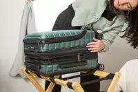 A person examines the zipper on the side of the Delsey Paris Shadow 5.0 Carry-on with Laptop Compartment